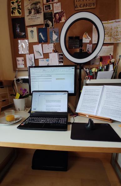 Fotografía de mi mesa de trabajo en estos momentos. En el centro de la mesa están un portátil abierto y detrás una pantalla extra con otra documentación. A la derecha del portátil hay un atril de madera con el Reglamento Delegado 2023/2772 (vamos, la traducción en español de los NEIS) abierto.
Hay un hueco libre a la derecha donde hay un plato con un zumo de naranja mediado, donde perfectamente cabría una pantalla más (si la tuviera)