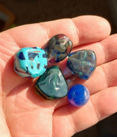 Image of several experimental glass beads held in a hand, palm open. Colors include shades of blue, green and purple.