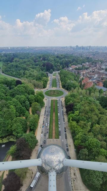 View from the viewing platform of the Atonium in Belgium. Big two way street and a roundabout. Greenery on both sides and Brussels in the distance.