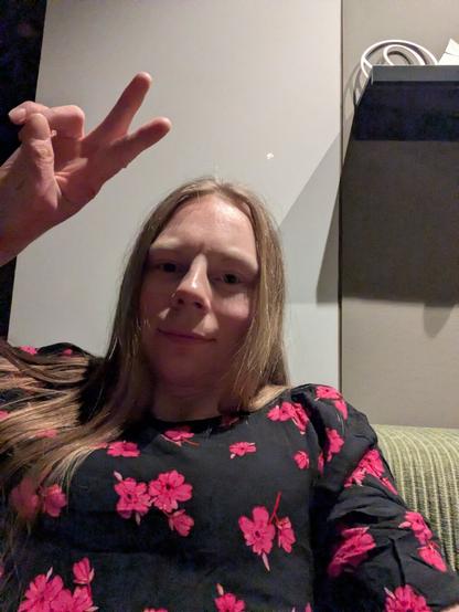 In a dimly lit room, a young woman in her mid-20s, poses for a selfie. She is seated on her green couch.