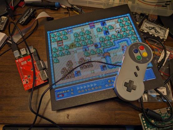 A bright pixelated LED panel shows the World 1 map in Super Mario Bros 3. A SNES style controller is sitting on top of the LED panel. On the right a red PCB with 3 connectors (2 occupied) can be seen. This is the "Active3" adapter. Under it (with just a few features visible, such as the USB ports) is a Pi 5. All around on the wood desk are pieces of electronics from those other projects I just never manage to tidy up...