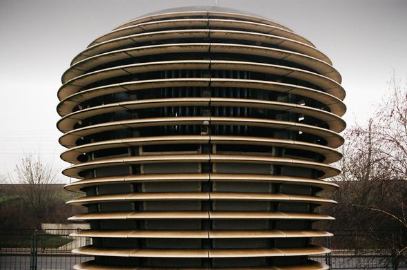 This image shows a large, round structure made up of stacked horizontal discs or layers. It resembles a modern architectural installation or sculpture, possibly designed for air filtration or environmental art purposes. The setting appears to be outdoors, possibly in an urban area.