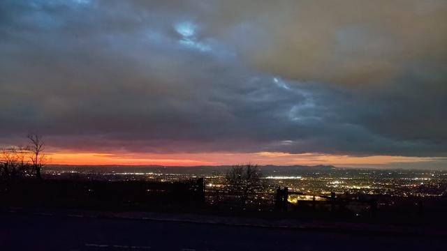 Looking over Cheltenham, from the side of a hill. The streetlights are twinkling. There is a band of red sky, on the horizon, where the sun has just set. The rest of the sky is dark and cloudy.