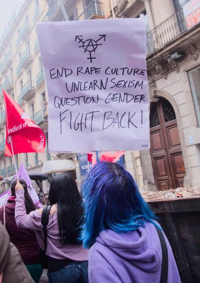Girl with blue hair and purple hoodie holding up a sign with Trans Anarchy sign and text ""END RAPE CULTURE, UNLEARN SEXISM, QUESTION GENDER, FIGHT BACK!"

Noia amb els cabells blaus i dessuadora lila sostenint un cartell amb el símbol de l'Anarquia Trans i el text "ACABEM AMB LA CULTURA DE LA VIOLACIÓ, DESAPRENEM EL SEXISME, QÜESTIONEM EL GÈNERE, REBEL·LEM-NOS!"