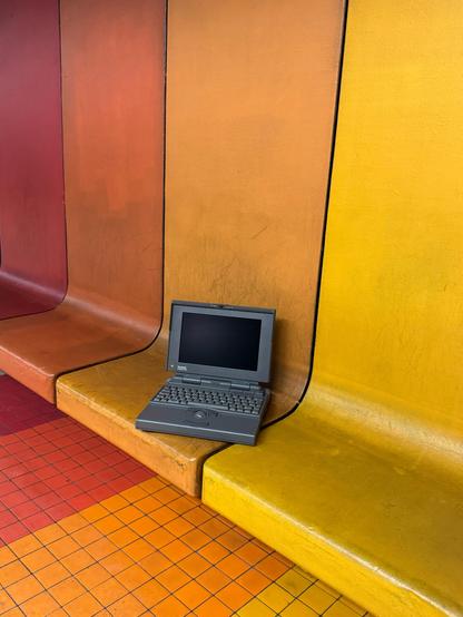 A PowerBook 145B on the red-orange-yellow colourful bench at Villa-Maria Métro station in Montréal.