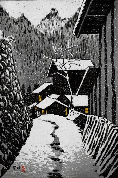 A view looking down a narrow lane in Minakami on a snowy winter's day. Tall stone foundations create a wall on our left; the blank side of a building stands on our right. The lane is deserted, but a rough track cleared in the snow on the ground tells of earlier foot traffic. Up ahead, more snow covers the rooftops of other buildings, and warm light glows in their windows. Beyond, snowy tree-covered mountains rise toward a dim, overcast sky. Snow continues to fall across the scene.