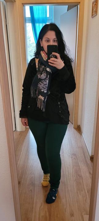 I'm a short woman in front of a mirror, shoulder length dark hair and dark eyes, pale skin. Wearing a scarf with cats, a black velvet cardigan with some charms sewn on it, dark green jeans and mismatched socks