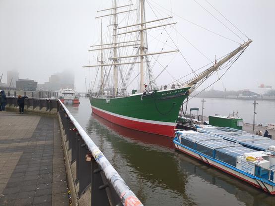 Ein Segelschiff mit grün-rotem Anstrich im Hafen liegend.