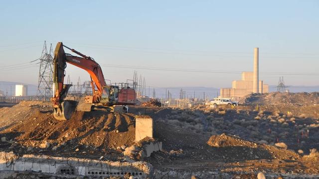 shot of a crane digging at the Hanford site with a reactor in the background