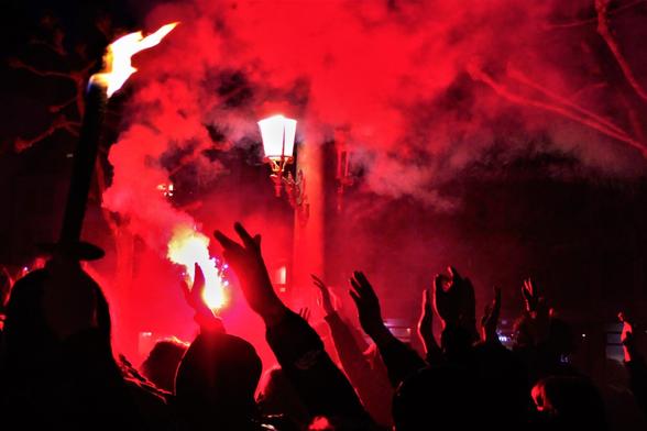 Les manifestant•es ont les mains en l'air pour scander "Siamo Tutti Antifascisti" Un fumigène rouge est allumé et éclaire la foule dans la nuit