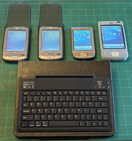 4 of my iPaqs lined up with the screens turned on.  Below them sits the Kensington Key Folio keyboard.  It is black, rubber, and has white lettering on the keys.