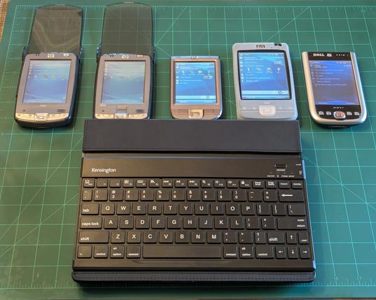4 of my iPaqs and my Dell Axim X51V lined up with the screens turned on.  Below them sits the Kensington iPad Key Folio Pro keyboard.  It is hard plastic and black in color. It has white lettering for the keys.