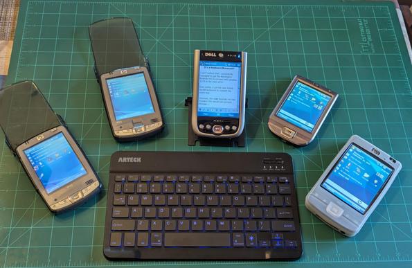 4 of my iPaqs and my Dell Axim X51V fanned out around the keyboard. In the middle of them sits the Arteck keyboard.  It is hard plastic and black in color. It has white lettering for the keys. The Dell Axim has Word Mobile loaded up.