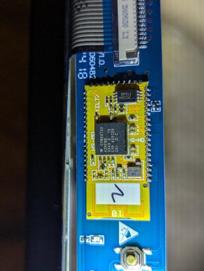 A shot from a different angle of the small rectangular circuit board inside the keyboard.  Its mostly blue and yellow and has a close up of the Bluetooth chip.