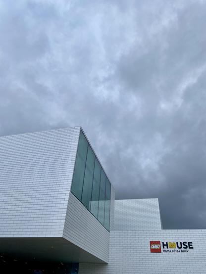 LEGO House in Billund, Denmark. A white building framed from large blocks. A dark cloudy sky hangs over it. It looks nice. We might get some rain!