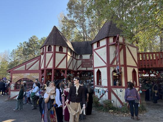A medieval-style pottery shop at a Renaissance fair, with red-and-white towers, handcrafted ceramics, and costumed visitors browsing.