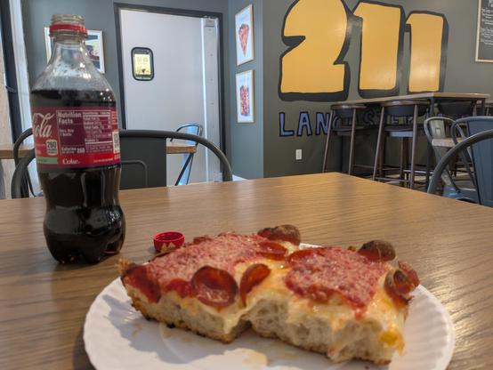 2 slices of Detroit style pizza with pepperoni on a paper plate. 211 mural on the wall in the background