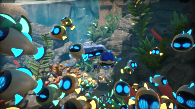 Several robots are underwater. Most of them are fish robots with a cute emoji face, and in the middle there's a little humanoid robot (the astro bot!). All of them are shining white with blue accents. They're all swimming together towards the camera