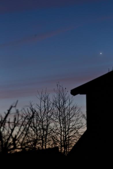 Foto des Abendhimmels mit rötlichen Zirruswolken. Im Vordergrund Bäume und ein Teil eines Hauses.