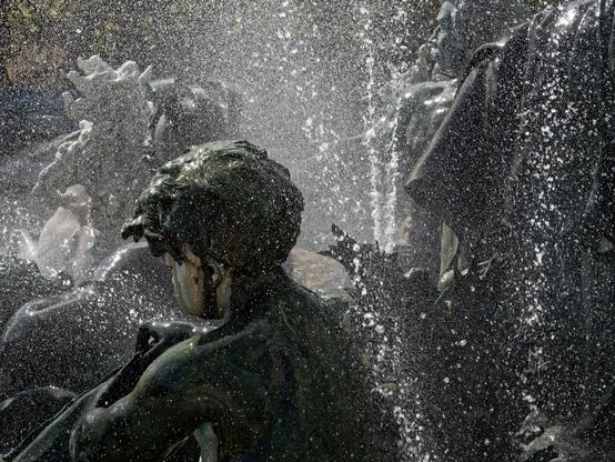 A dynamic fountain scene featuring intricate bronze sculptures surrounded by splashing water. The contrast between the solid, timeless statues and the ever-moving droplets creates a sense of energy and motion. The image evokes themes of mythology, nature, and the passage of time, blending permanence with transience in a captivating display.
