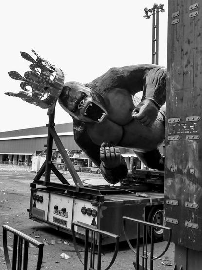 A large gorilla with a crown on its head and fists on its chest is protruding from an urban feature. It's a decorative element from a funfair ride on the side of a lorry.