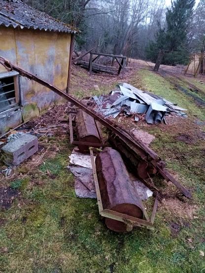 A set of three agricultural rollers connected with chains and a towing hitch that is flipped over backwards to save space. They're dented but functional. Each roller is mounted in a steel frame. They're in a yard next to a bunch of metal junk.