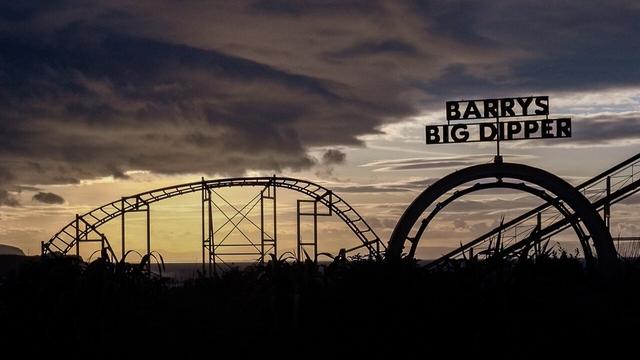 a fairground roller coaster silhouette against a dramatic evening sky. large letters say "Barry's Big Dipper"