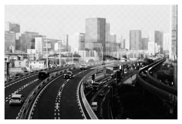 Black and white photograph through a window with a Rhombus structure. You can see six lanes of cars, four on a bridge and two below. Next to it are the tracks of the Tokyo Monorail and some of the city's skyscrapers in the background.