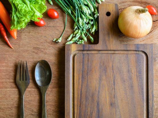 A dark wooden cutting board surrounded by fresh vegetables.