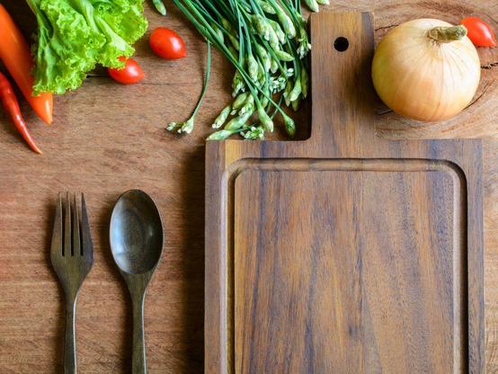 A dark wooden cutting board surrounded by fresh vegetables.