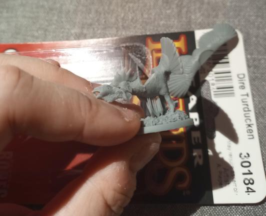 Miniature of a chimeric creature with the tail of a turkey, wings of a duck, and body of a chicken. It has all 3 of those heads too. Under the neck on the model there's a little bundle of vertical supports characteristic of 3D resin printing.