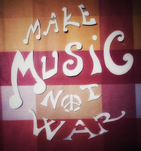 Letters cut out from a sheet of paper, placed on an orange-red checkered pattern, which form the text: make music not war.