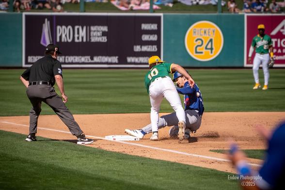Dodger James Outman slides safely into third base, as the ball hits his back and Athletics infielder Max Muncy is unable to apply the tag.