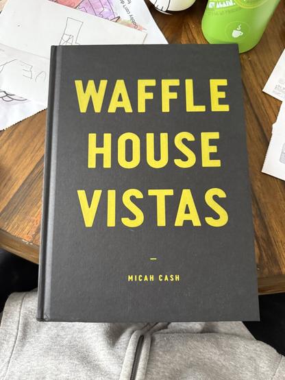 Large black book with bold yellow print that says "Waffle House Vistas” sitting on a dining room table.