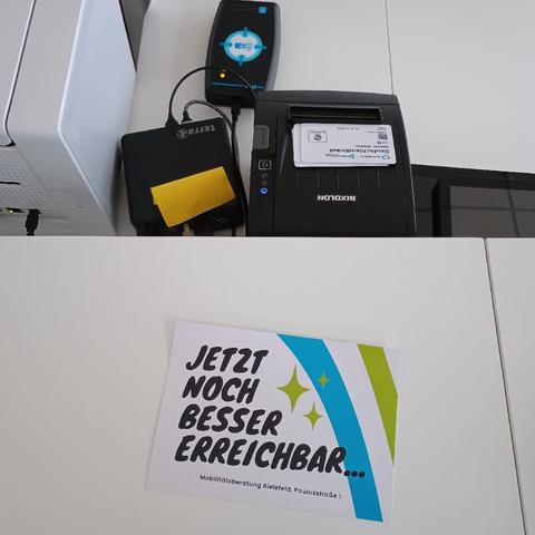 Foto weiße Theke mit Flyer: "Jetzt noch besser erreichbar... Mobilitätsberatung Bielefeld, Paulusstraße 1"

Dahinter Mini-PC, Chipkarten-Rohlinge, Eticket-NFC-Gerät, Chipkarten-Drucker.