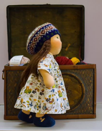 A handmade waldorf-inspired doll with long brown hair wearing a cotton dress with an autumn mice pattern.  She is wearing a Fair Isle Tam or beret
