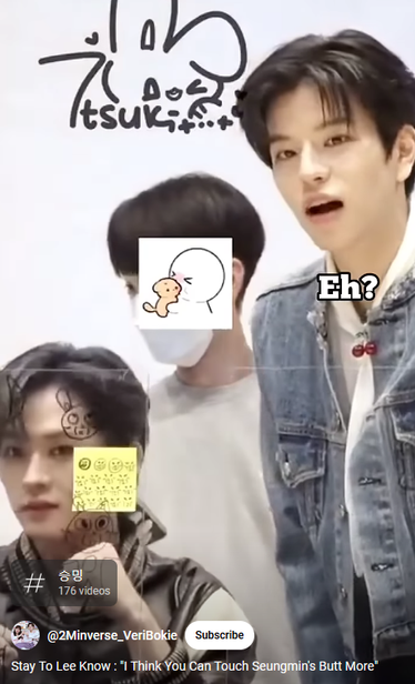 Seungmin stands and looks inquisitively at the audience, with his mouth open. Caption over Seungmin: Eh?

Lee Know is sitting next to Seungmin, with his fists raised like he's ready to fight, but also perking up with interest and a little smile.

In the background there's a person with a graphic pasted over their face (staff member??)