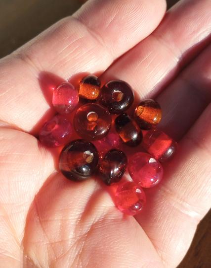 Image of a batch of handmade lampwork glass beads in shades of red and amber, held in an open palm.
