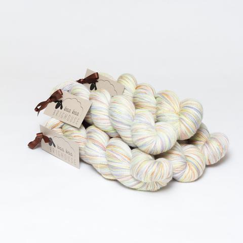Picture shows a pyramid of five skeins of yarn positioned diagonally. The yarn is various shades of red, yellow, purple , green and white.