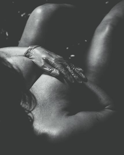 The image is a black and white photograph of a person with a gloved hand touching their shoulder. The composition and lighting give it a dramatic and artistic feel.