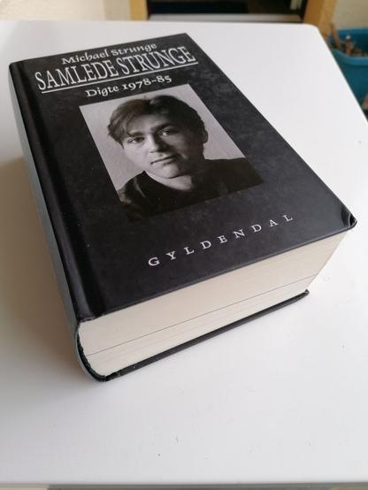 Ein schwarzes Buch mit dem Titel "Samlede Strunge, Digte 1978-85" mit dem Gesamtwerk von Michael Strunge. Das Cover zeigt ein schwarz-weißes Portraitfoto des Autors.