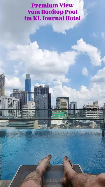 POV Foto von der Liege am Pool: Füße sichtbar, dahinter Pool, dahinter Skyline von Kuala Lumpur