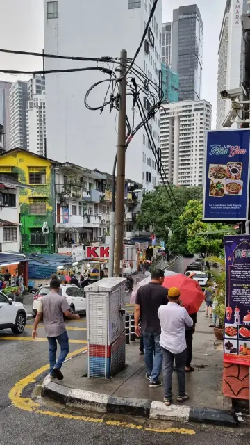 Foto auf einer Straße in Bukit Bintang mit vielen Menschen und Autos. Am Haus links ist Street Art sichtbar.