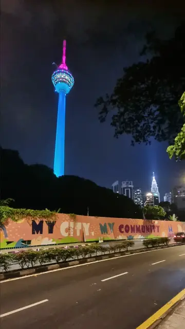 Foto: Zwei in der Nacht beleuchtete Türme. Im Vordergrund eine Wand mit Streetart, Aufschrift "My City. My Community" (MY ist das Länderkürzel für Malaysia)