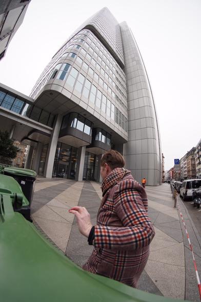 ich, In meinem rot braunen karierten Mantel, wie ich vor der Kamera weg laufe. Im Hintergrund das Hochhaus der deutschen Bahn in Frankfurt.
