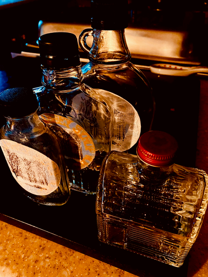 Color image of glass syrup bottles ready to be filled with fresh maple syrup. Image shows several clear labeled bottles ready to be filled with syrup.