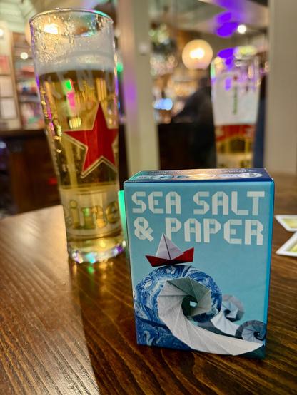 Sea Salt and Paper game box. Behind it are a couple of pints of lager on a pub table.