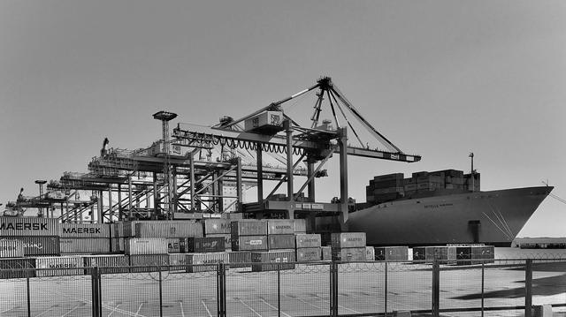 A black and white Photo taken at Container terminal Bremerhaven. It  shows container gantry cranes with a ship at the quay wall.