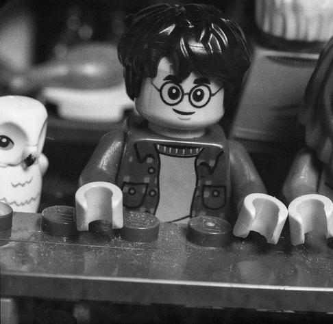 Macro shot of a Lego Minifig of Harry Potter with his owl sitting at a table of the Lego Great Hall of Hogwarts model
