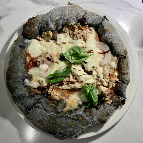 Charcoal dough pizza with tomato sauce, garlic, rabbit meat, mozzarella, onions and fresh basil.